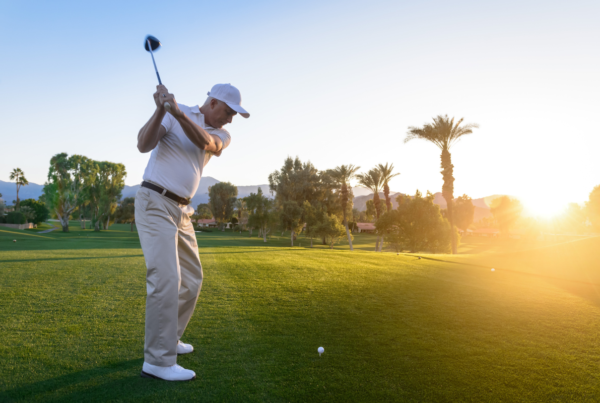a man in white tees off on a putting green on a golf course at sunrise