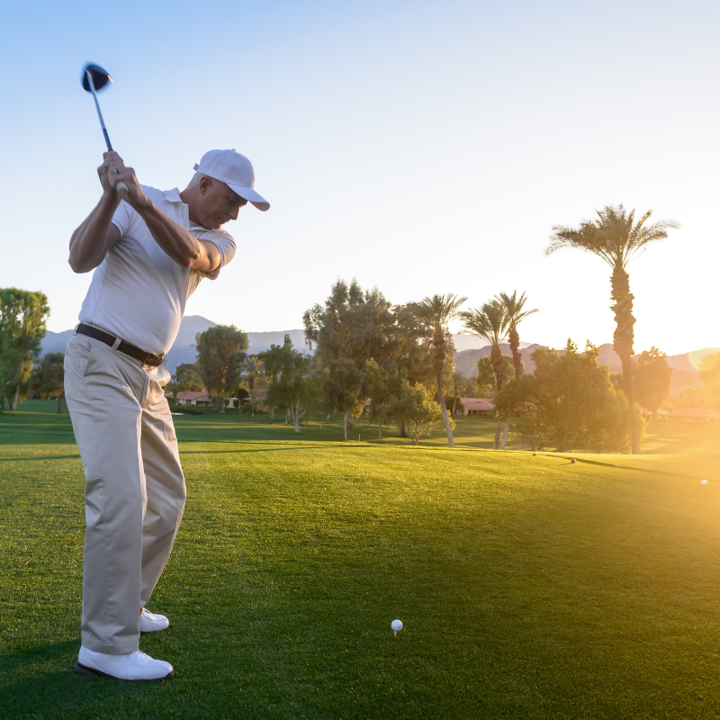 a man in white tees off on a putting green on a golf course at sunrise