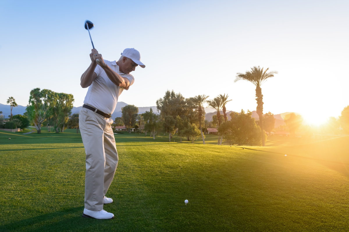 a man in white tees off on a putting green on a golf course at sunrise